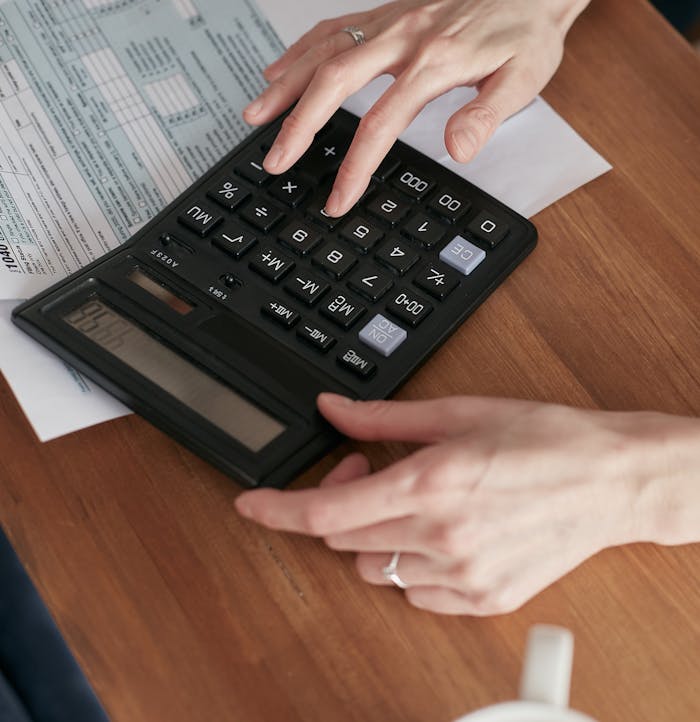 services-02 Person calculating finances with a calculator and document on a wooden desk.