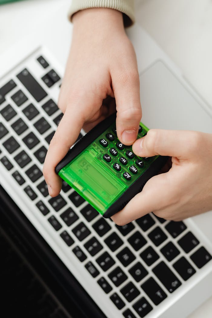 services-04 Hands operating a green calculator over a laptop keyboard in an indoor setting.